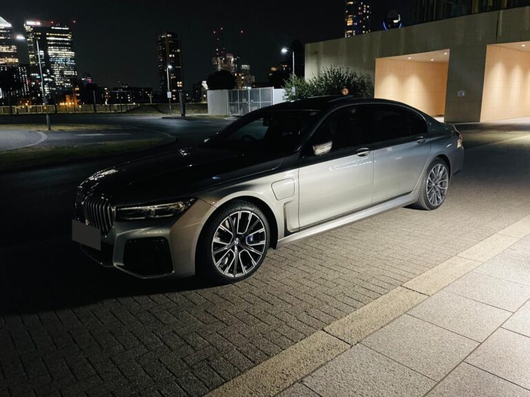 BMW 7 Series chauffeur car parked at night, with city lights behind
