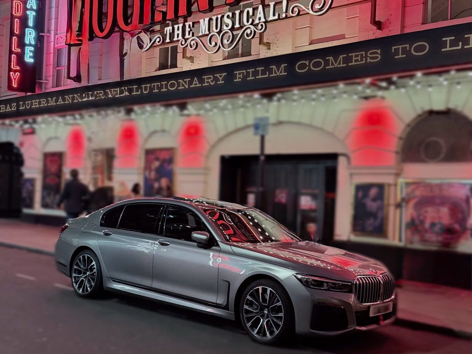 Silver BMW 7 Series chauffeur car parked at night outside a West End theatre in London