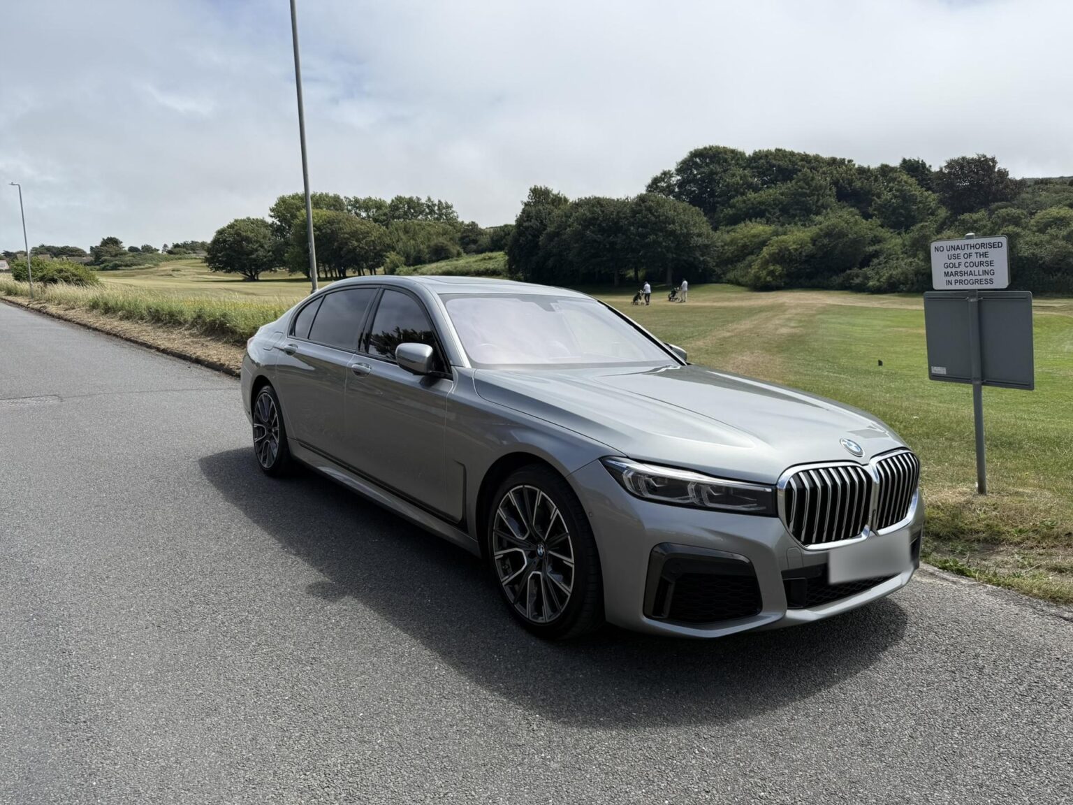 Grey BMW 7 Series chauffeur car on a road beside a golf course