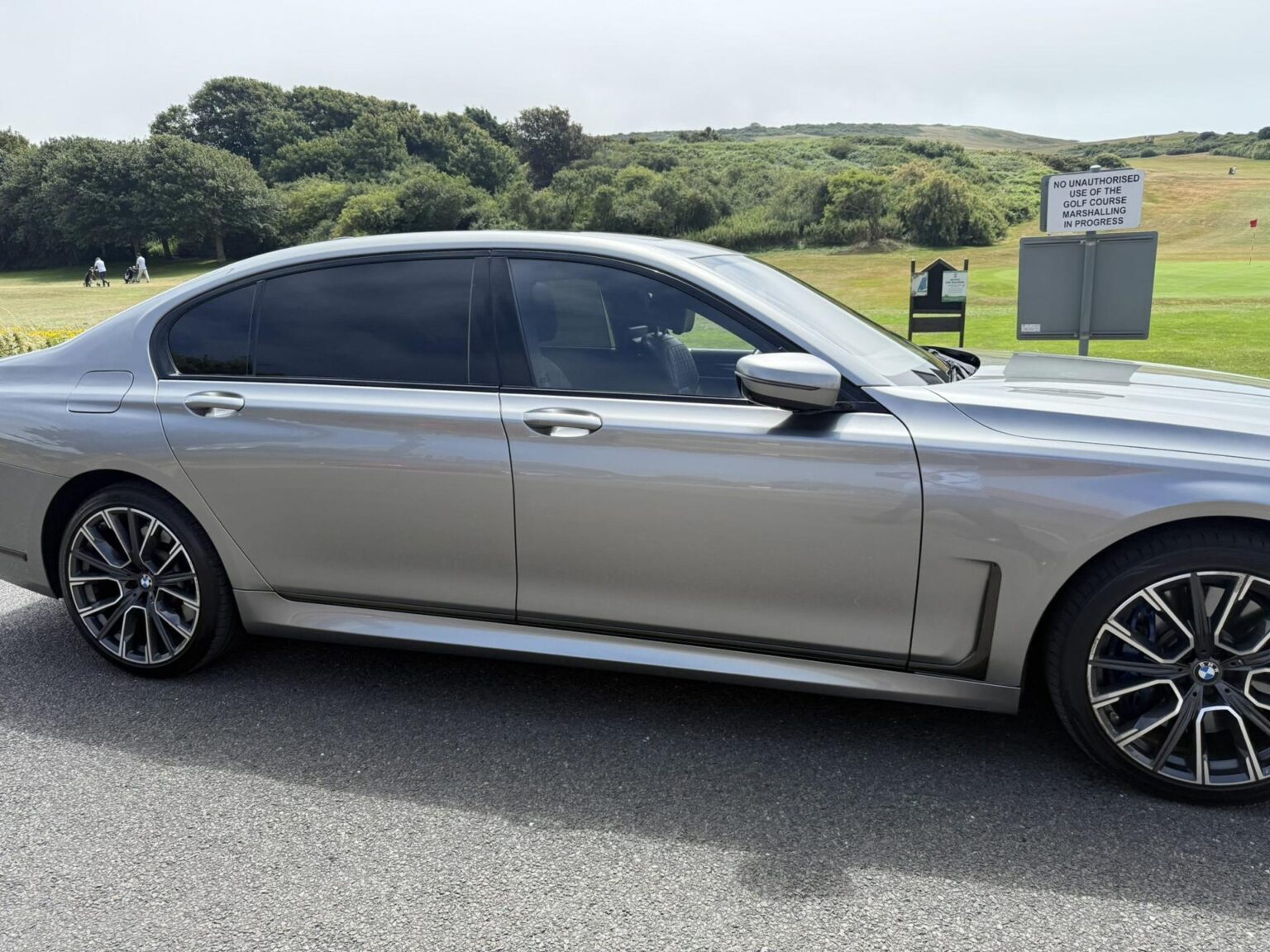 Grey BMW 7 Series chauffeur car, side profile, by a golf course on the Sussex coast