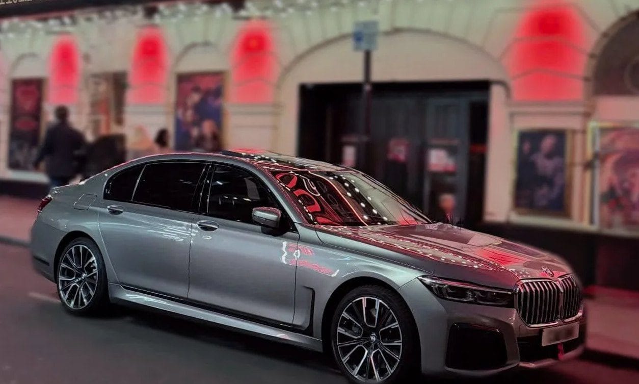 BMW 7 Series chauffeur car waiting outside the Piccadilly Theatre in London at night