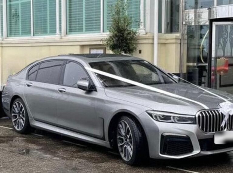 Silver BMW 7 Series wedding car dressed with white ribbons, parked outside a venue