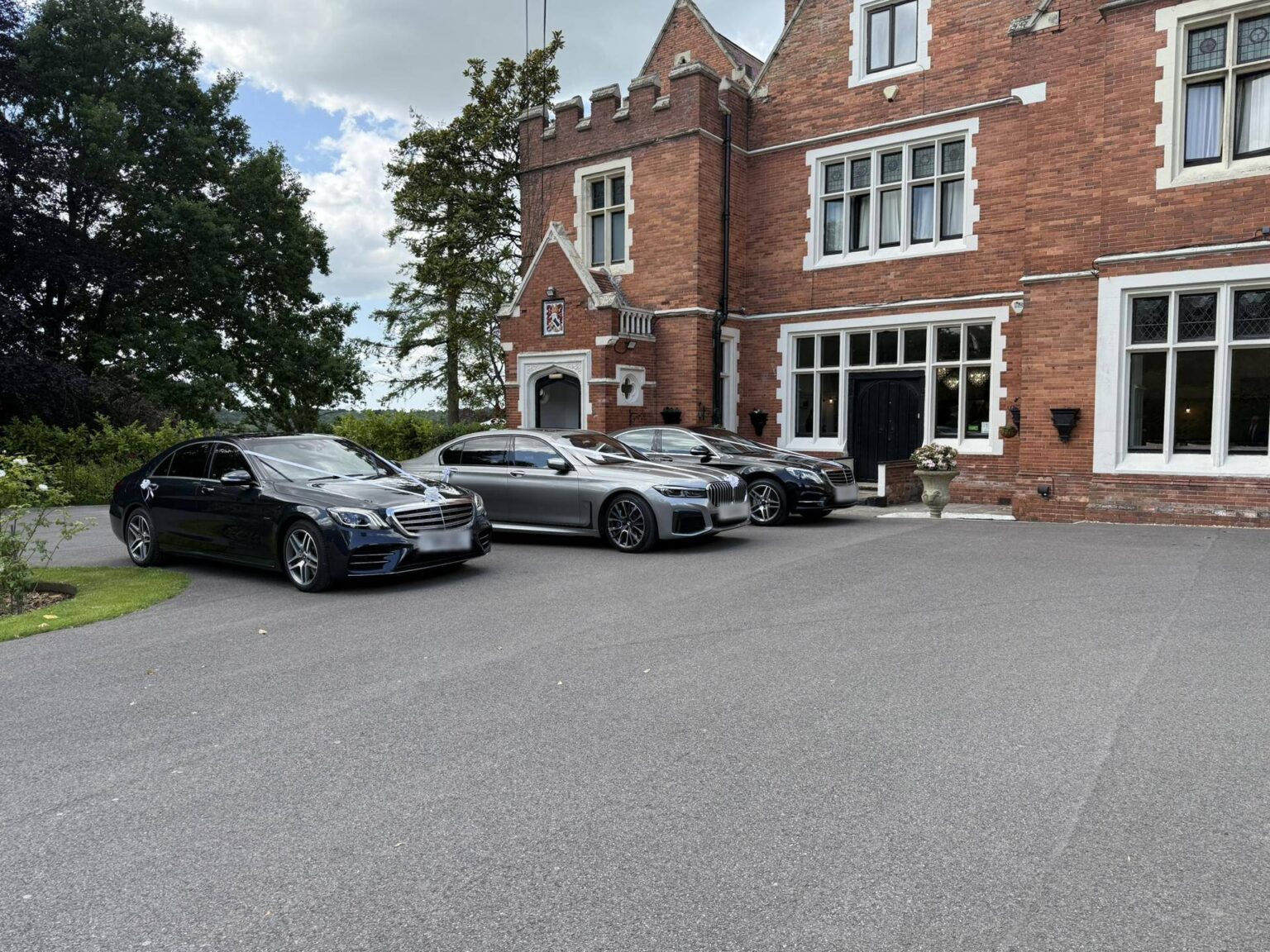 Three chauffeur-driven executive cars lined up outside a red-brick country house